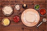 Phases of making a pizza - stretching the dough on wooden plate, top view with ingredients on a table