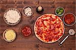 Phases of making a pizza - spreading tomato sauce on the dough, top view with ingredients on a table