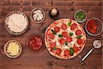 Phases of making a pizza - the ready to bake pizza with ingredients around on a table, top view