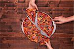 Hands taking pizza slices off the baking pan - top view, copy space