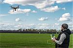 man operating of flying drone quadrocopter at the green field.