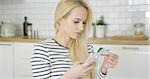 Young girl in striped shirt holding phone and card making purchase in Internet while sitting in kitchen.