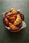 Freshly baked croissants in a wicker basket on the dark green background. Delicious Breakfast