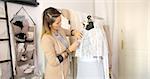 Young female tailor in casual clothing standing near mannequin and sewing dress on it in parlour.