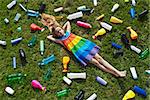 Sad little girl lying on the garbage filled grass - plastic pollution concept