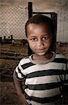 Young African boy standing in a township, looking at camera