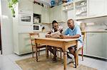 Young African couple sit together in a kitchen, reading a newspaper