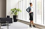 Young confident businesswoman looking through office window