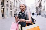 Stylish mature female shopper looking at smartphone on street, Florence, Italy