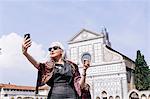 Stylish mature woman taking selfie in front of Santa Maria Novella church, Florence, Italy