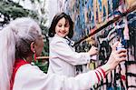 Mature woman and girl spray painting graffiti wall together