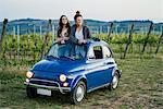 Tourists standing through car sunroof, vineyard, Tuscany, Italy