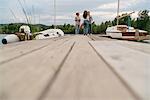 Three friends on pier, beside boat, relaxing, holding bottles of beer, low angle view