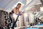 Young woman training, pedalling exercise bike in gym