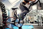 Neck down view of young woman training, pedalling exercise bike in gym