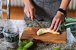 Hands of young woman slicing banana at kitchen table