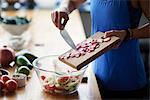 Mid section of young woman at kitchen table preparing sliced radish