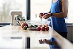 Mid section of young woman at kitchen table crumbling feta into salad bowl