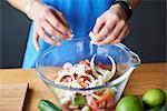 Hands of young woman at kitchen table crumbling feta into salad bowl