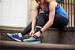 Young female runner sitting outside front door fastening trainer laces
