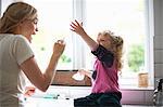 Mother and daughter in kitchen, daughter sitting on work surface playing with washing up bubbles