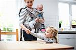 Young girl helping mother lay table, mother carrying baby boy in sling