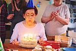 Senior woman blowing out candles on birthday cake at party