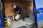 Man working in a brewery, loading metal beer kegs into a van.