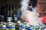 Man working in a brewery, cleaning metal beer kegs with a high pressure washer.
