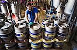 Man working in a brewery, stacking metal beer kegs.