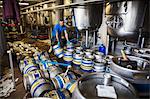 Man working in a brewery, carrying metal beer kegs.