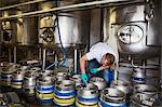 Man working in a brewery, closing metal beer kegs.