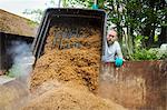 Man pouring spent grain into a large container, steam rising, during the brewing process.