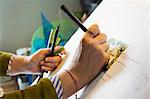 Close up of woman sitting at a drawing board, drawing with a fine liner pen, using a design template.