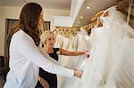 Two women, a young bride to be and a mature sales assistant looking through rails of wedding dresses.