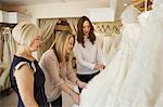 Three women, a client and two retail advisors in a wedding dress shop, looking through the choice of gowns.
