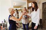 A young woman holding a champagne glass and clinking her glass with two women, celebrating the choice of wedding dress in a bridal shop.