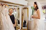 A woman, a bride to be, trying on dresses with the help of a sales assistant, in a wedding dress shop.