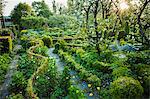 View of garden with stone path, flower beds, shrubs and trees in the background.