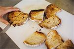 Close up high angle view of person cutting slices of toasted bread in half with a knife.