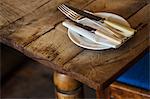 Close up high angle view of plate with knives and fork and a serviette on a rustic wooden table.