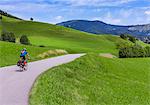 Man riding bike on road through grass fields