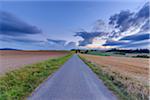 Countryside with harvested cereal field and paved laneway at dusk in summer at Roellbach in Spessart hills in Bavaria, Germany