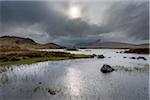 Moor landscape with a river and the sun glowing through dense cloudy sky at Rannoch Moor in Scotland, United Kingdom