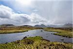 Moor landscape with a river and the sun shining through the cloudy sky at Rannoch Moor in Scotland, United Kingdom