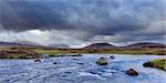 River in moor landscape with dark storm clouds and mountains in the background at Rannoch Moor in Scotland, United Kingdom