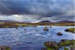 River in moor landscape with dark storm clouds with mountains in the background at Rannoch Moor in Scotland, United Kingdom