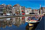 Typical buildings line the street with a tour boat moored along the seawall of the Oudezijds Voorburgwal canal in Amsterdam, Holland