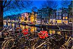 Typical buildings line the canal with a row of bicycles parked along the Herengracht in the evening in Amsterdam, Holland