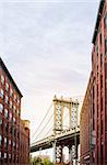Manhattan Bridge between Manhattan and Brooklyn over East River seen from a narrow alley enclosed by two brick buildings on a sunny day, New York City